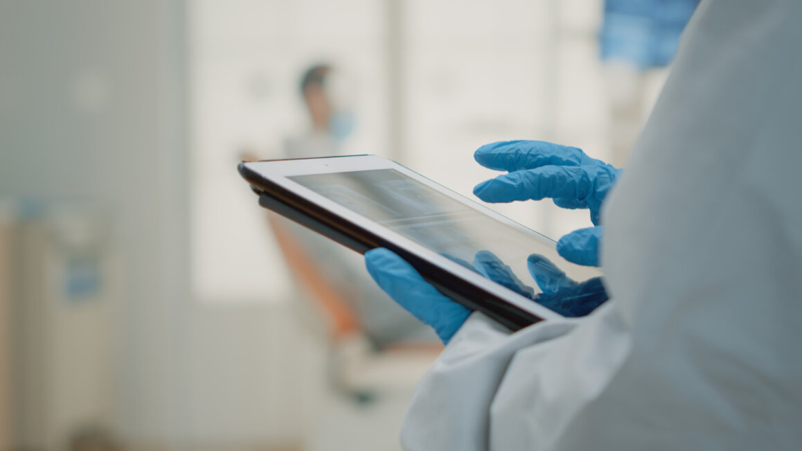 Close up of dentist's hand using dental xray on tablet at oral health appointment.